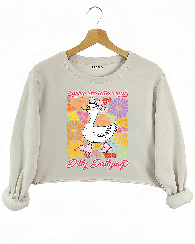 Ragglo beige crop sweatshirt featuring a cute duck in pink rain boots and a bow, surrounded by vibrant flowers, with 'Sorry I'm Late I Was Dilly Dallying' text, perfect for playful floral-inspired casual wear.

