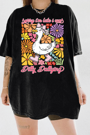 Ragglo black tee featuring a cute duck in pink rain boots and a bow, surrounded by vibrant flowers, with 'Sorry I'm Late I Was Dilly Dallying' text, perfect for playful floral-inspired casual wear.

