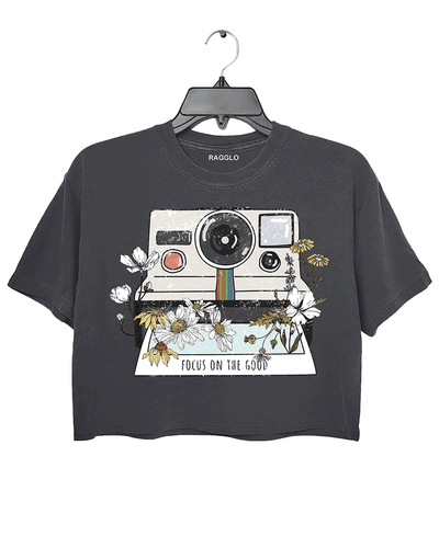 Ragglo dark gray crop top featuring a vintage Polaroid camera surrounded by flowers, with 'FOCUS ON THE GOOD' text, perfect for retro-inspired streetwear with a positive vibe.

