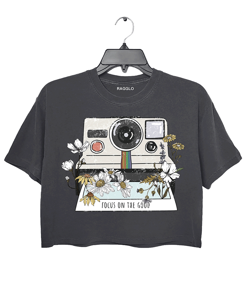 Ragglo dark gray crop top featuring a vintage Polaroid camera surrounded by flowers, with 'FOCUS ON THE GOOD' text, perfect for retro-inspired streetwear with a positive vibe.

