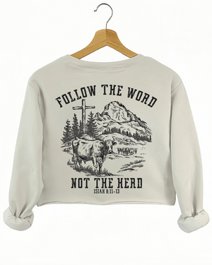 Ragglo beige women's crop sweatshirt back featuring a mountain landscape with cattle, a cross, and trees, and the text 'Follow The Word Not The Herd' and 'Isaiah 8:11-13' in a spiritual graphic design.