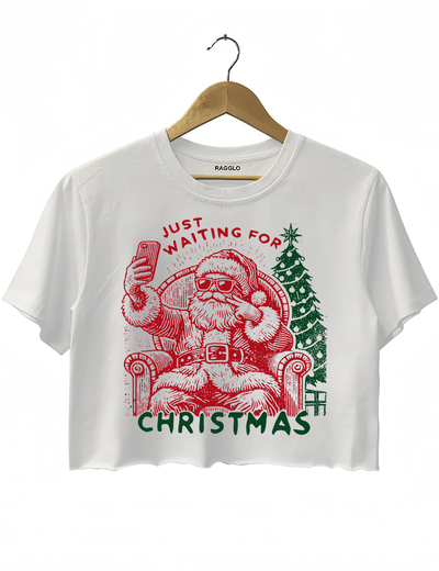 Ragglo white crop top featuring a Santa selfie graphic with sunglasses, a Christmas tree, and 'JUST WAITING FOR CHRISTMAS' text, perfect for festive holiday streetwear and fun celebrations.

