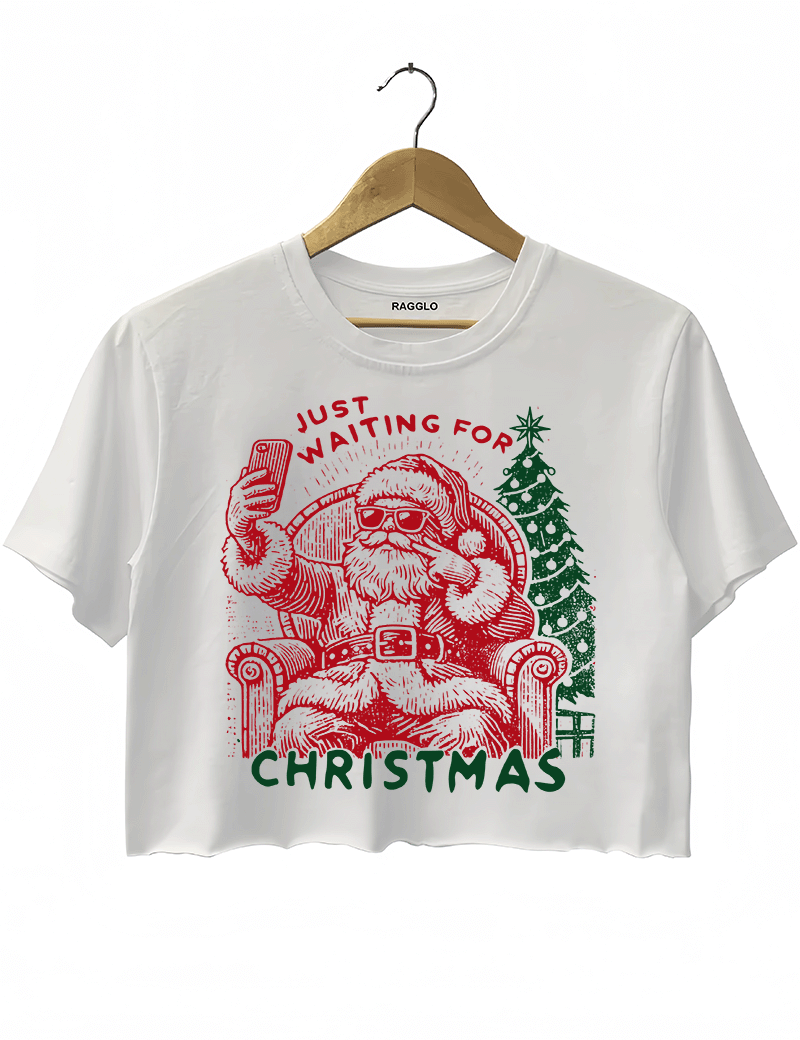 Ragglo white crop top featuring a Santa selfie graphic with sunglasses, a Christmas tree, and 'JUST WAITING FOR CHRISTMAS' text, perfect for festive holiday streetwear and fun celebrations.

