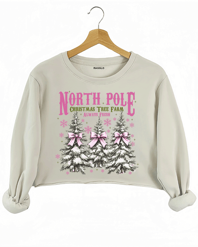 Ragglo beige crop sweatshirt featuring three Christmas trees with pink bows and snowflakes, with 'NORTH POLE CHRISTMAS TREE FARM ALWAYS FRESH' text, perfect for festive holiday streetwear.

