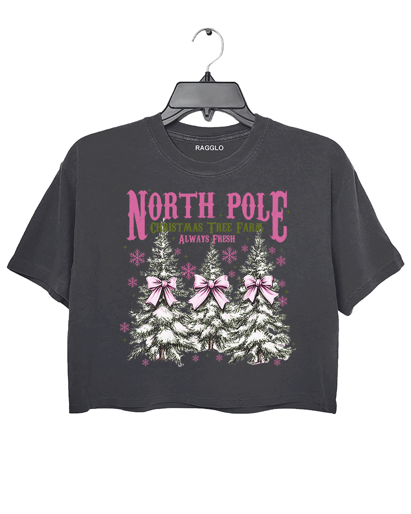 Ragglo dark gray crop top featuring three Christmas trees with pink bows and snowflakes, with 'NORTH POLE CHRISTMAS TREE FARM ALWAYS FRESH' text, perfect for festive holiday streetwear.

