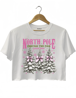 Ragglo white crop top featuring three Christmas trees with pink bows and snowflakes, with 'NORTH POLE CHRISTMAS TREE FARM ALWAYS FRESH' text, perfect for festive holiday streetwear.

