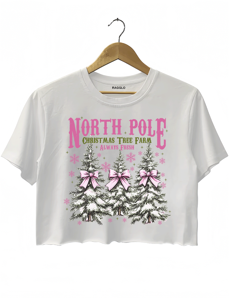 Ragglo white crop top featuring three Christmas trees with pink bows and snowflakes, with 'NORTH POLE CHRISTMAS TREE FARM ALWAYS FRESH' text, perfect for festive holiday streetwear.

