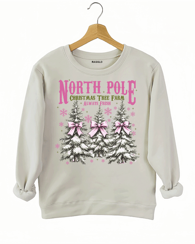 Ragglo beige sweatshirt featuring three Christmas trees with pink bows and snowflakes, with 'NORTH POLE CHRISTMAS TREE FARM ALWAYS FRESH' text, perfect for festive holiday streetwear.

