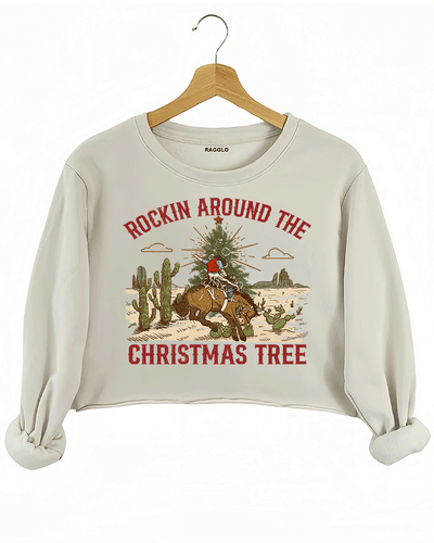 Ragglo beige crop sweatshirt featuring a cowboy riding a horse with a Christmas tree in a desert scene with cacti, with 'ROCKIN AROUND THE CHRISTMAS TREE' text, perfect for festive western-style streetwear.

