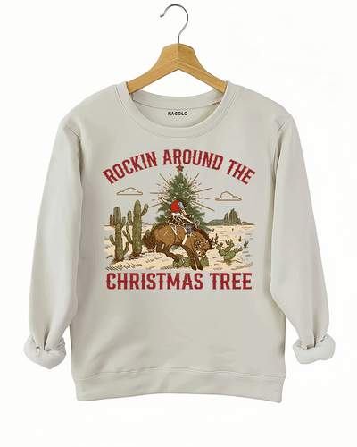 Ragglo beige sweatshirt featuring a cowboy riding a horse with a Christmas tree in a desert scene with cacti, with 'ROCKIN AROUND THE CHRISTMAS TREE' text, perfect for festive western-style streetwear.

