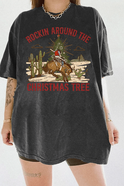Ragglo dark gray tee featuring a cowboy riding a horse with a Christmas tree in a desert scene with cacti, with 'ROCKIN AROUND THE CHRISTMAS TREE' text, perfect for festive western-style streetwear.

