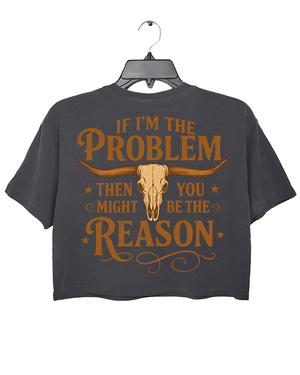 Dark gray crop top with the text 'IF I'M THE PROBLEM THEN YOU MIGHT BE THE REASON' in bold orange font across the back, accompanied by a bull skull illustration.