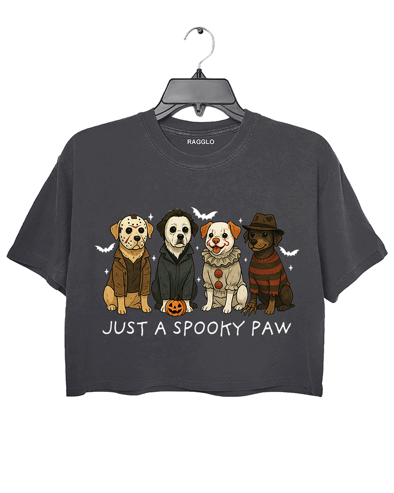 Dark gray cropped T-shirt by RAGGLO featuring four cartoon-style dogs dressed as iconic horror movie characters—Michael Myers, Freddy Krueger, Pennywise, and Billy the Puppet. Surrounded by flying bats and a small jack-o'-lantern, with the playful phrase "JUST A SPOOKY PAW" printed below. Perfect for Halloween or casual streetwear with a spooky twist.