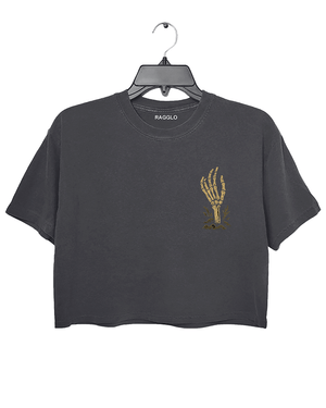 Front view of a dark gray cropped Halloween T-shirt by RAGGLO, featuring a minimalist gold skeleton hand graphic holding a flame on the left chest. Subtle yet spooky, ideal for a low-key Halloween vibe.