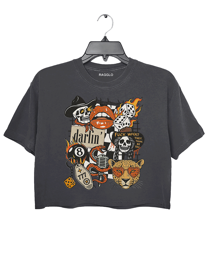 Dark gray crop top featuring a bold graphic design with various motifs, including a flaming skull, a dice with number 8, a red lip with teeth, a leopard's face, and the word 'darlin' in cursive. The design also includes the phrase 'FUCK WHAT THEY THINK' and a few additional skulls and vintage-style elements, combining punk and retro aesthetics.