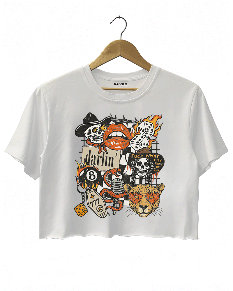 White crop top featuring a bold graphic design with various motifs, including a flaming skull, a dice with number 8, a red lip with teeth, a leopard's face, and the word 'darlin' in cursive. The design also includes the phrase 'FUCK WHAT THEY THINK' and a few additional skulls and vintage-style elements, combining punk and retro aesthetics.