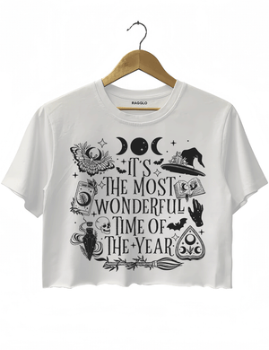 Ragglo white crop top featuring witchy elements like moons, bats, a witch hat, spellbook, and potion bottle, with 'IT’S THE MOST WONDERFUL TIME OF THE YEAR' text, perfect for magical Halloween streetwear.

