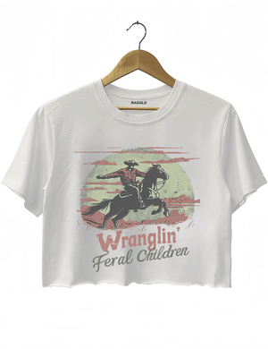 Ragglo white women's crop top featuring a cowboy riding a horse under a moonlit mountain background with the humorous text 'Wranglin' Feral Children' in a playful western graphic design.