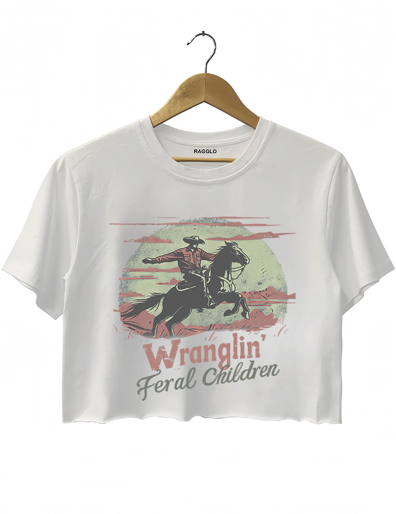 Ragglo white women's crop top featuring a cowboy riding a horse under a moonlit mountain background with the humorous text 'Wranglin' Feral Children' in a playful western graphic design.