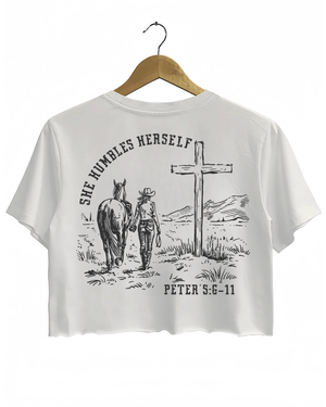 White Ragglo women's crop t-shirt with 'She Humbles Herself' text, a cowgirl walking with a horse, a cross, and Peter 5:6-11 scripture, perfect for Christian and western-style apparel.

