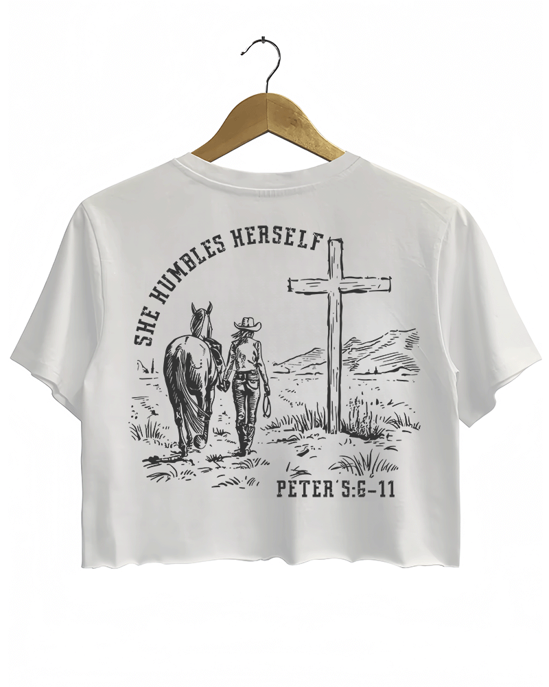 White Ragglo women's crop t-shirt with 'She Humbles Herself' text, a cowgirl walking with a horse, a cross, and Peter 5:6-11 scripture, perfect for Christian and western-style apparel.

