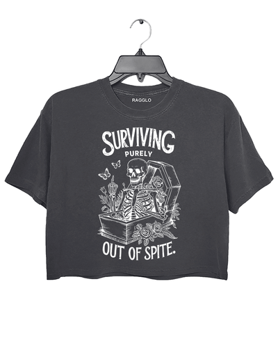Dark gray crop top featuring a skeleton sitting in a coffin with roses, butterflies, and candles, alongside the humorous text 'Surviving Purely Out of Spite,' available on Ragglo.