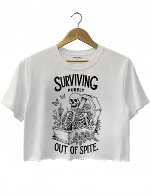 White crop top showcasing a skeleton inside a coffin with floral accents and butterflies, paired with the bold phrase 'Surviving Purely Out of Spite,' available on Ragglo.