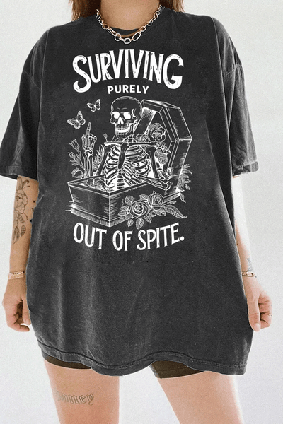 Dark gray T-shirt displaying a skeleton reclining in a coffin, surrounded by roses and butterflies, with the rebellious text 'Surviving Purely Out of Spite,' available on Ragglo.