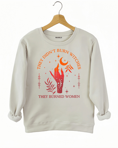 Beige sweatshirt with "They Didn't Burn Witches, They Burned Women" graphic featuring a celestial hand, stars, moon, and plants.