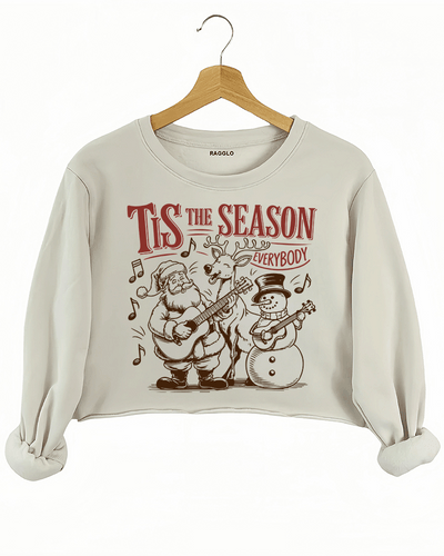 Christmas graphic with the text Tis The Season Everybody, featuring Santa, a reindeer, and a snowman playing guitars, surrounded by musical notes, printed on a beige crop sweatshirt available at Ragglo.