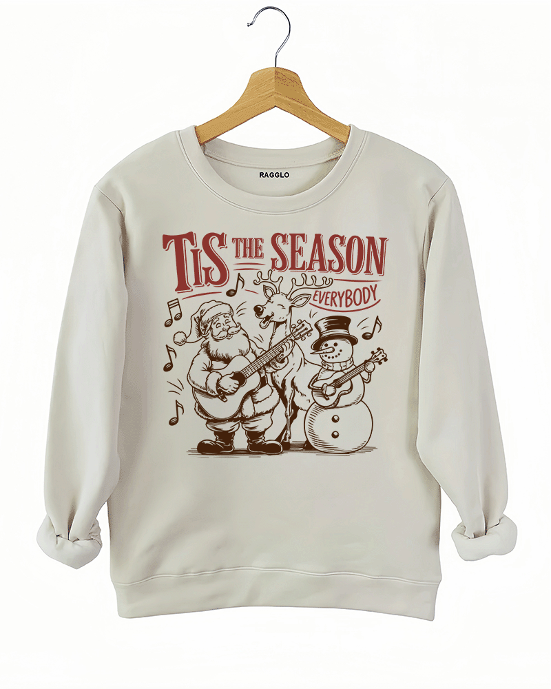 Tis The Season Everybody holiday graphic with Santa, a reindeer, and a snowman playing guitars, with music notes around them, printed on a beige sweatshirt available at Ragglo.