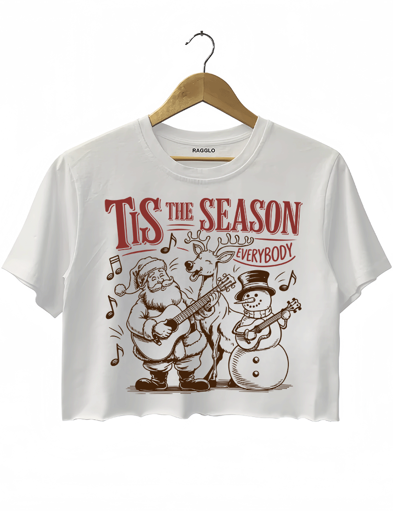 Christmas-themed Tis The Season Everybody graphic showing Santa, a reindeer, and a snowman joyfully playing guitars surrounded by music notes, printed on a white crop top available at Ragglo.