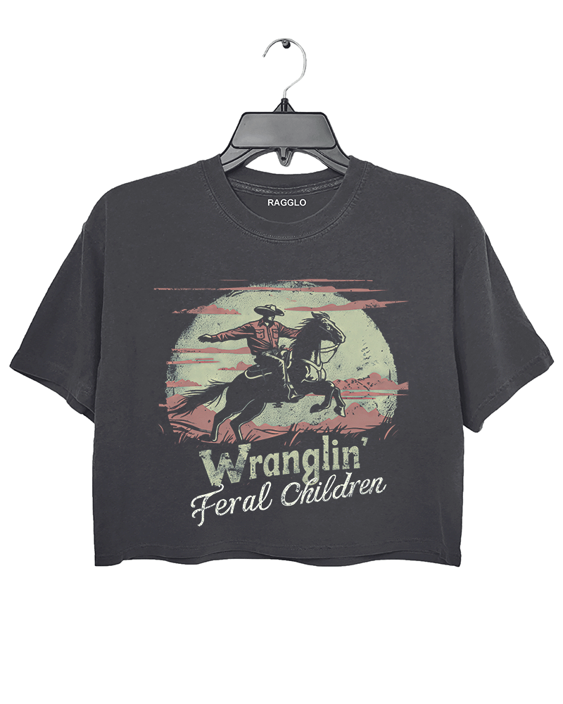 Ragglo dark gray crop top featuring a vintage-style cowboy graphic with the humorous text 'Wranglin' Feral Children,' depicting a cowboy on horseback in a desert scene.