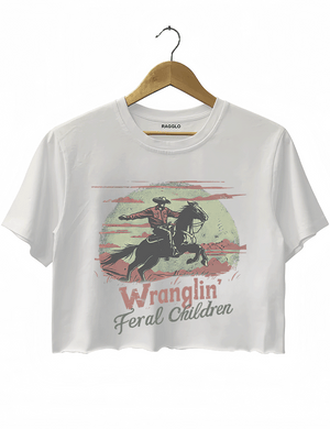 Ragglo white crop top featuring a vintage-style cowboy graphic with the humorous text 'Wranglin' Feral Children,' showcasing a cowboy riding a horse under a pale, textured moon.