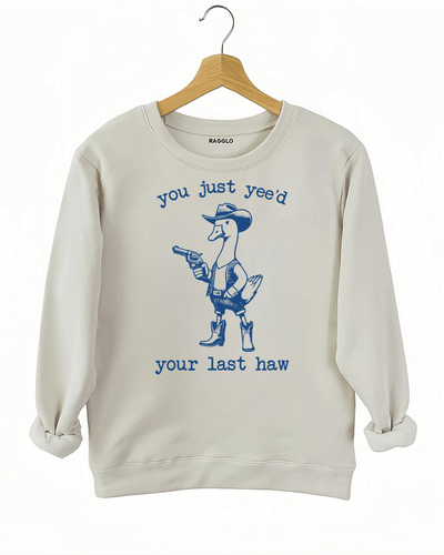 Humorous western-style duck design with a cowboy outfit and the text 'You Just Yee’d Your Last Haw' on a beige sweatshirt, available on Ragglo.