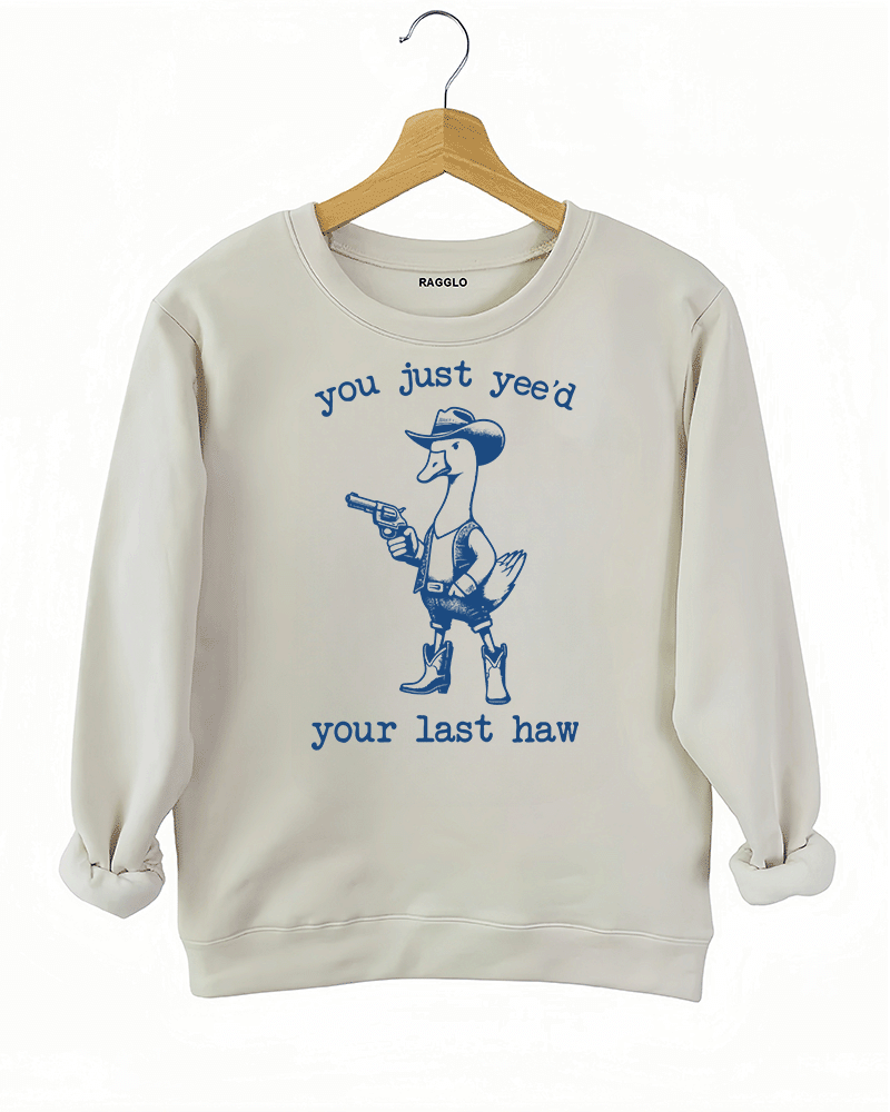 Humorous western-style duck design with a cowboy outfit and the text 'You Just Yee’d Your Last Haw' on a beige sweatshirt, available on Ragglo.