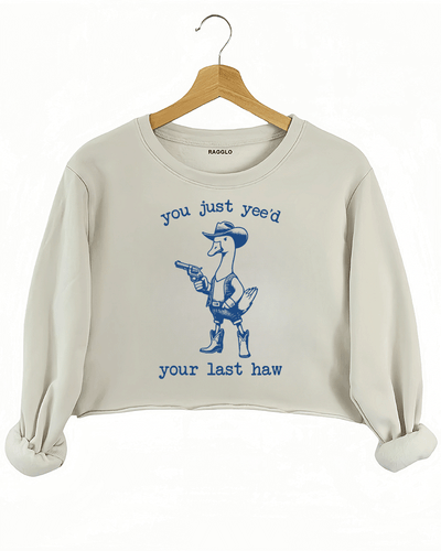Funny design featuring a cowboy duck with a revolver and the text 'You Just Yee’d Your Last Haw' on a beige crop sweatshirt, available on Ragglo.