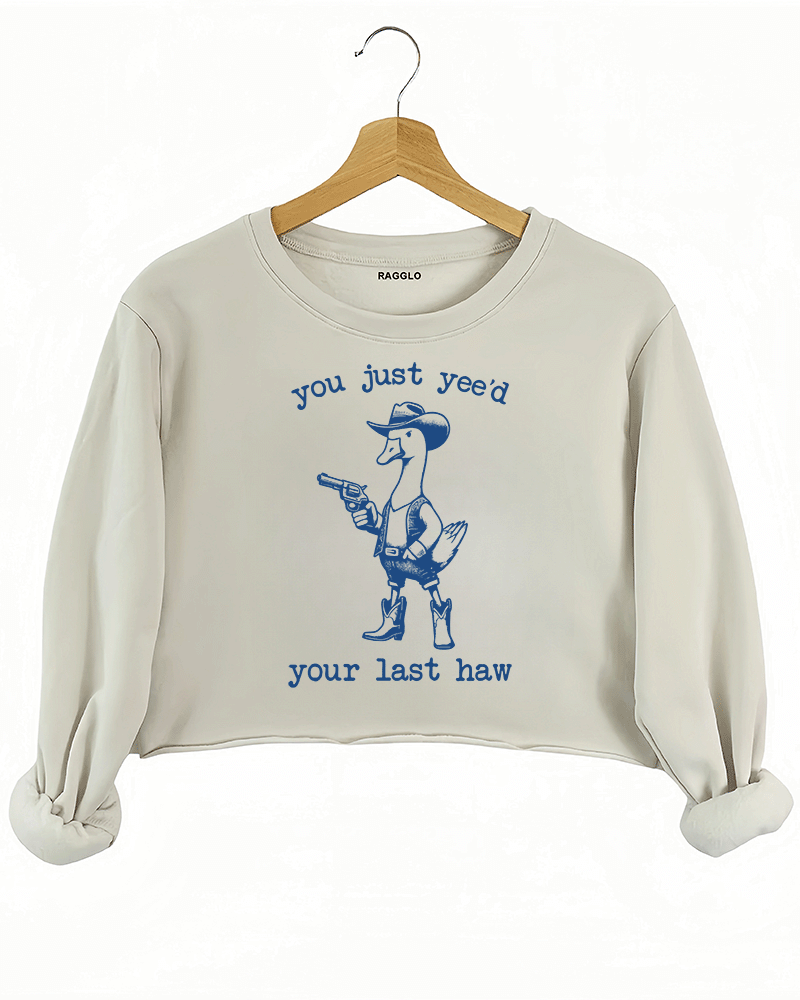 Funny design featuring a cowboy duck with a revolver and the text 'You Just Yee’d Your Last Haw' on a beige crop sweatshirt, available on Ragglo.
